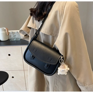 Detail of a matte black leather saddle bag with a plush charm on a beige trench coat