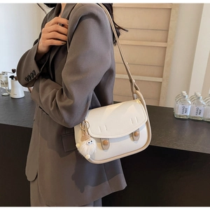 Detail view of cream saddle bag with brown snap buttons and a cute plush monster charm