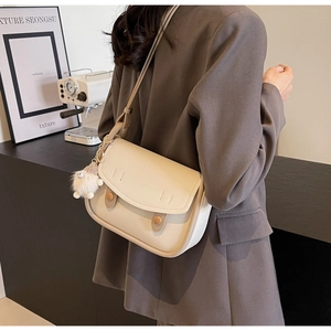 Detail view of cream-white saddle bag with decorative brown buttons and a plush sheep charm