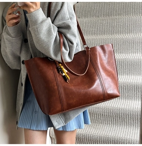 Close-up of brown textured leather tote bag with unique ethnic beaded charm accessory