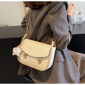 Detail view of cream saddle bag with brown decorative buttons and cute white plush charm
