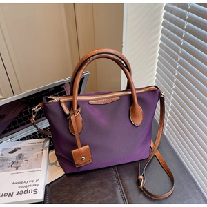 Detail der lila Nylontasche mit braunen Ledergriffen und Markenanhänger auf Ledertisch