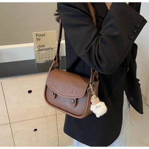 Close-up of vintage brown saddle bag with plush doll charm on a chic black blazer