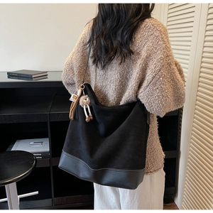 Detail view of a large black suede tote bag with plush charm on a model in knitwear
