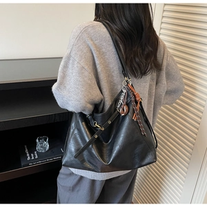 Close-up of a large black faux leather tote bag with stylish knot charm on a model