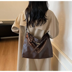 Detailed view of deep brown faux leather tote with metallic buckle and woven charm