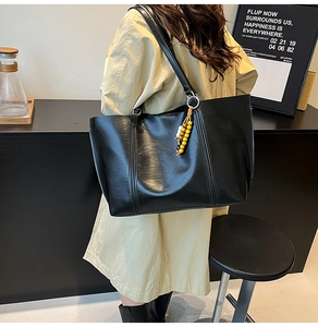 Detail of black leather tote bag featuring vertical stitching and colorful beaded charm
