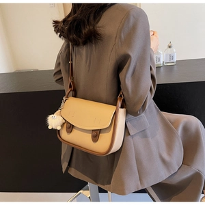 Detail of beige saddle bag with brown leather trim and cute plush charm on shoulder strap