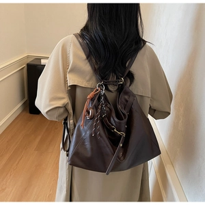 Detail of dark brown leather tote bag with braided orange cord and metal chain accents