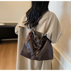 Deep brown leather tote bag with braided charm shown as a shoulder bag on a model