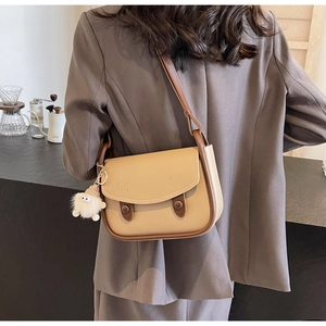 Detail of a chic two-tone flap crossbody bag with a cute plush charm on a café background