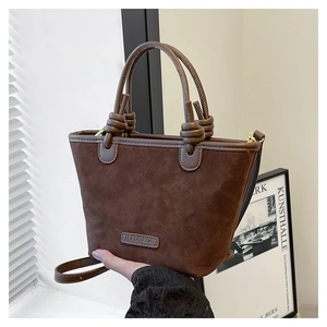 Detail of dark brown suede bucket bag featuring knotted handles and brand leather patch