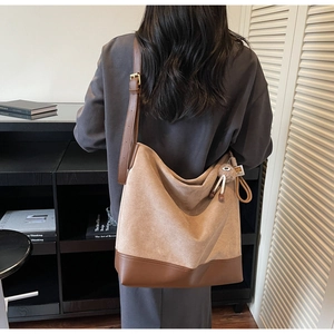 Detail view of a large two-tone bucket bag featuring suede texture and leather strap