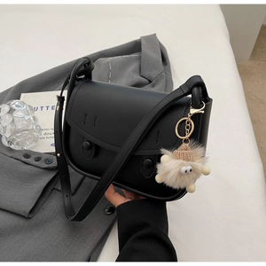 Detailed view of black leather saddle bag with cute plush monster charm on gray blazer