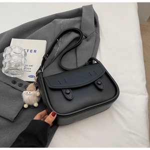 Detail of a black leather saddle bag featuring a decorative monster plush charm on its side