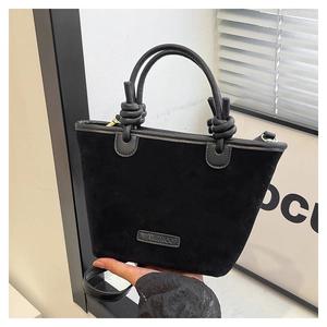 Close-up of black suede bucket bag featuring a twisted handle and elegant metal logo plaque