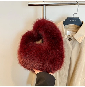 Close-up of burgundy plush faux fur tote bag held by hand against a trench coat background