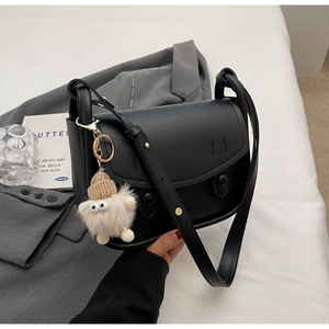 Detail of black leather saddle bag with matte finish and cute plush monster charm