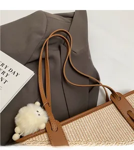 Detail der geflochtenen Strohtasche mit braunen Lederriemen und weißem Bommel-Anhänger
