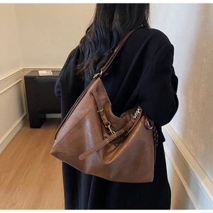 Detail view of brown leather tote bag with silver letter pendant and textured finish