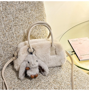 Detail of plush beige faux fur handbag featuring a cute long-eared rabbit charm accessory