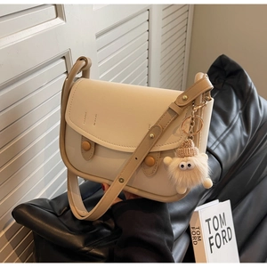 Detail of cream saddle bag with brown adjustable strap and cute monster plush pendant