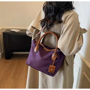 Detail der lila Nylon-Beuteltasche mit braunen Ledergriffen in wohnlicher Umgebung