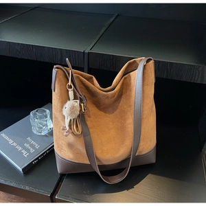 Detail view of large brown suede tote bag with plush charm and smooth leather handles