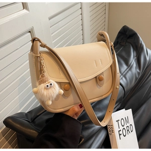 Close-up of beige saddle bag with decorative round buttons and cute plush monster charm