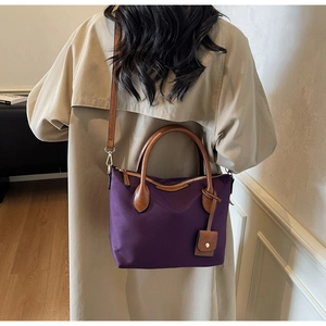 Detailansicht einer lila Nylontasche mit Ledergriffen an einem Model im beigen Mantel