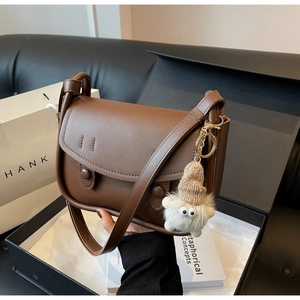 Detailed close-up of a brown matte leather saddle bag featuring a cute plush monster charm