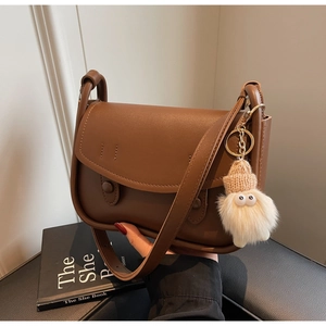 Brown faux leather saddle bag with cylindrical detail and cute plush charm accessory
