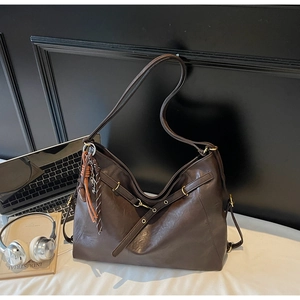 Detail of dark brown tote bag showing leather texture, golden buckle and woven knot charm