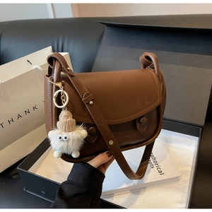 Detail of brown leather saddle bag with white plush monster charm in premium gift box set