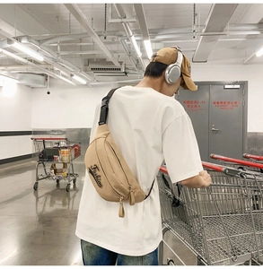Détail d'un sac bandoulière kaki avec inscription Fashion porté par un mannequin en extérieur