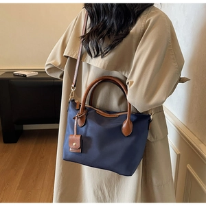 Detailansicht der marineblauen Nylon-Beuteltasche mit braunen Ledergriffen und Goldbeschlägen