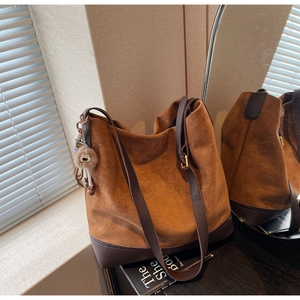 Detail view of brown suede tote bag with leather base and decorative charm pendant