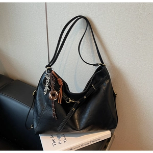 Detail of black faux leather tote bag with metal rings and donut pendant accessory