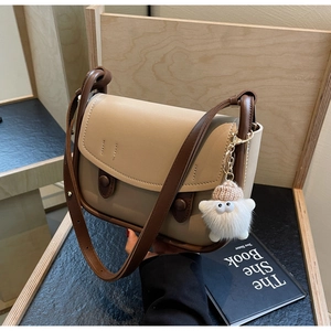 Detail of beige and brown saddle bag featuring golden hardware and a cute plush charm