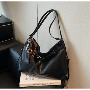 Close-up of black leather tote bag featuring a decorative silver forever charm and accessories