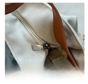 Detailed close-up of smooth metal zipper on canvas tote bag with brown handles