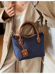 Dunkelblaue Nylon-Eimertasche mit braunem Lederbesatz getragen von Model im Trenchcoat