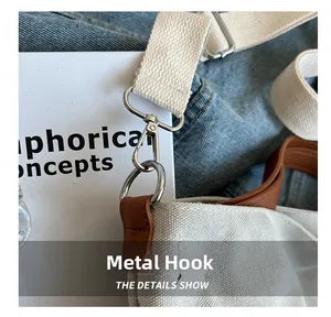 Detail view of silver metal hooks and brown leather reinforcement on a white canvas bag