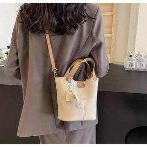 Detail of minimalist cream leather bucket bag with brown contrast strap worn cross-body