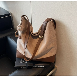 Detail of suede tote bag with leather straps and fur ball charm on leather chair
