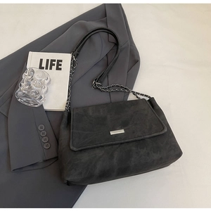 Detailansicht der dunkelgrauen Cord-Schultertasche mit Metalllogo und Kettenriemen auf Blazer