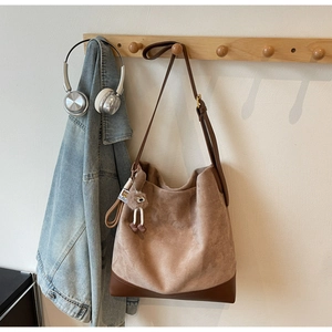 Detail of camel suede bucket bag with leather straps and cute bear charm on a hook