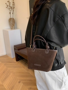 Minimalist deep brown suede bucket bag with dual handles and long shoulder strap