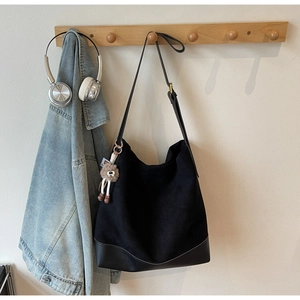 Detail of black suede hobo tote with smooth leather base and charm pendant