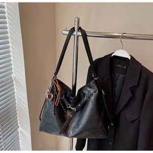 Detail of black faux leather tote bag featuring a decorative donut charm and slim shoulder straps